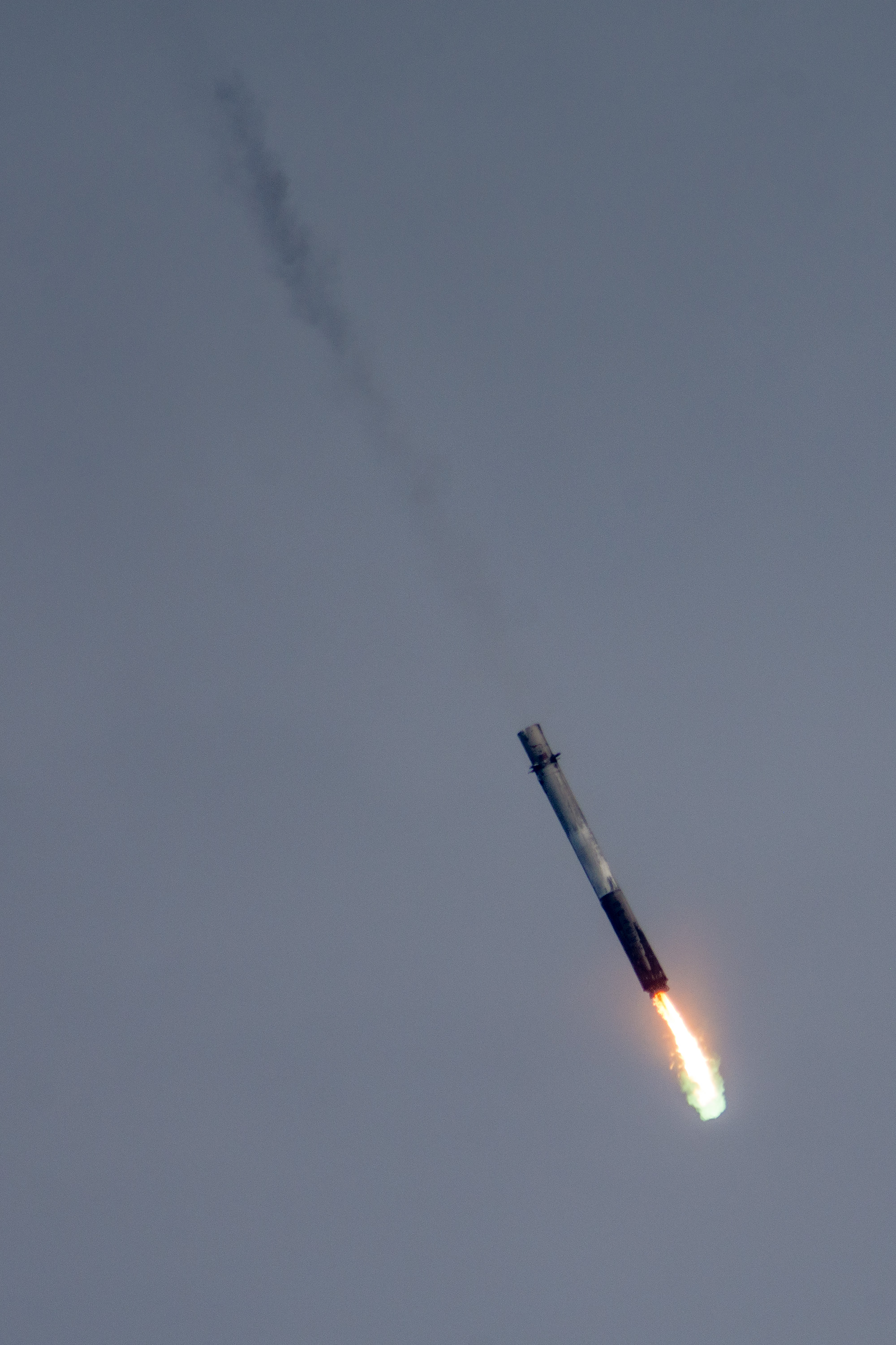 CRS-11's first stage relights its engines for the landing burn above Landing Zone 1. Green flame is visible from the pyrophoric starter, TEA-TEB